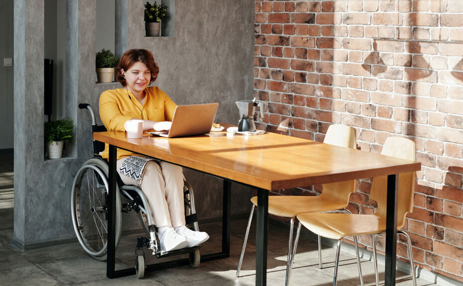 A woman in a wheelchair sits at a table working at a laptop